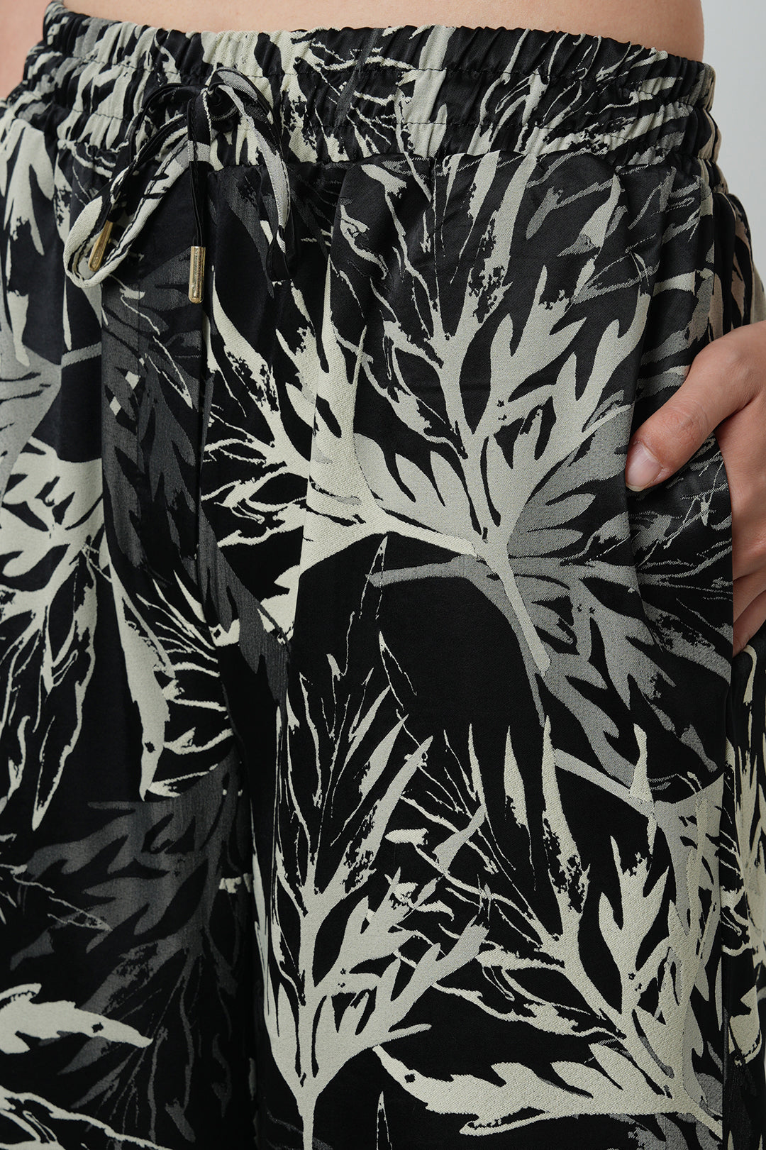 Toptan siyah yaprak desenli oversize saten kadın pantolon – bol paça, lastikli bel yapısı ve şık kumaşıyla günlük ve tesettür giyime uygundur.